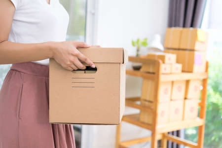Young asian girl freelancer business private working at home office holding packaging sort box delivery online market on purchase orders to customer.の写真素材