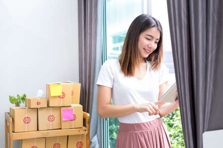 Young asian girl freelancer business private working at home office with holding tablet, laptop, note, packaging delivery online market on purchase or checking orders to customer.の写真素材