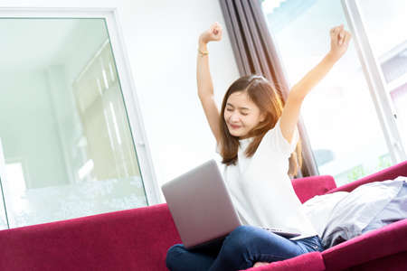 Young asian girl freelance lazy and happy success, finish, complete after working with laptop computer project in morning on sofa at home office in holidays.の写真素材