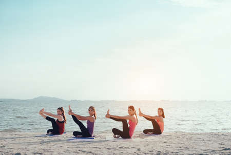 Young group man and woman yoga practice on mat relaxation in class exercise with pose fitness sport for healthy on the beach and seaside  modern city at sunrise relaxの写真素材