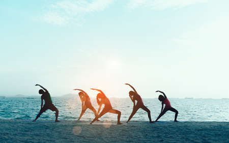 Young group man and woman yoga practice on mat relaxation in class exercise with pose fitness sport for healthy on the beach and seaside  modern city at sunrise relax holiday vacation time in summer.の写真素材