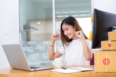 Young asian girl freelancer small business private working at home office with laptop, note, coffee, packaging delivery online market on purchase orders to customer.の写真素材