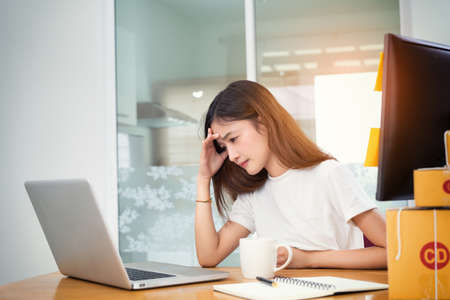 Young asian girl freelancer small business serious working at home office with laptop, note, coffee, packaging delivery online market on purchase orders to customer.の写真素材