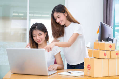 Young asian girl together teamwork freelancer small business private working at home office with laptop, note, phone, packaging delivery online market on purchase checking orders to customer.の写真素材
