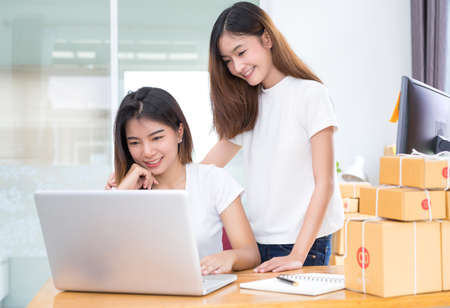 Young asian girl together teamwork freelancer small business private working at home office with laptop, note, phone, packaging delivery online market on purchase checking orders to customer.の写真素材