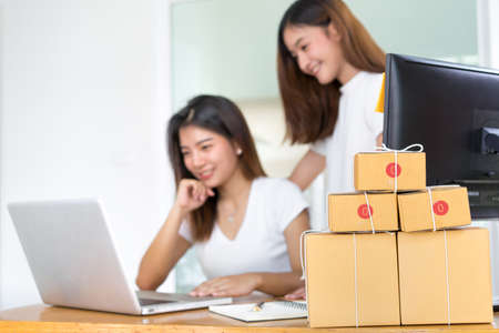 Young asian girl together teamwork freelancer small business private working at home office with laptop, note, phone, packaging delivery online market on purchase checking orders to customer.の写真素材