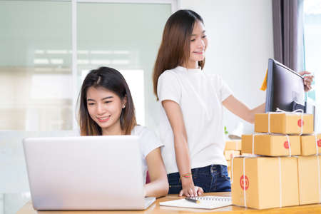 Young asian girl together teamwork freelancer small business private working at home office with laptop, note, phone, packaging delivery online market on purchase checking orders to customer.の写真素材