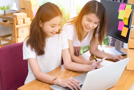 Young asian girl together teamwork freelancer business private working at home office with laptop, note, mobile, packaging delivery online market on purchase checking orders to customer.の写真素材
