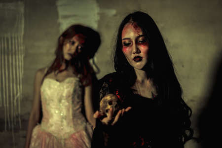 Witch death the ghost holding skull and zombie in dress women with blood skin is screaming darkness and nightmare background, horror of scary fear on hell is monster devil girl in halloween festival conceptの写真素材