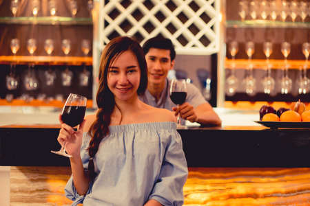 Young asian couple together man and woman cink glasses drink wine, cocktail in bar luxury party celebration clam relaxing in nightclub at pubの写真素材