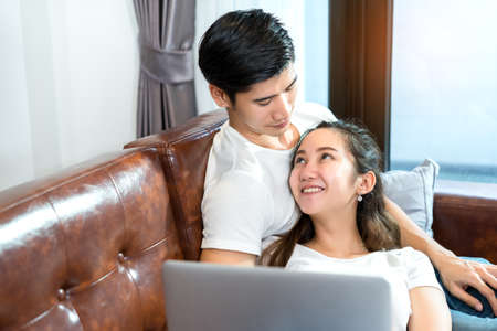 Young couple together man and woman looking laptop computer happy and smile relaxing on sofa in living room at home in holidays weekendの写真素材