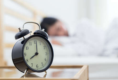 Closeup alarm clock, Young asian woman sleeping on the bed in the early morning and late work time...