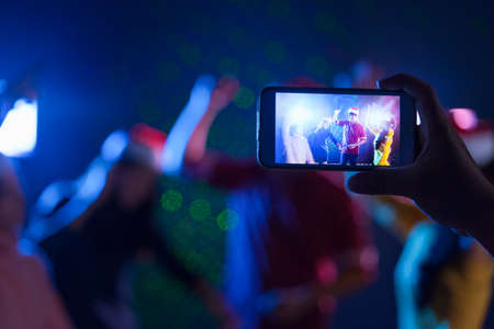 Right hand holding smartphone camera snap shot photo memories people christmas party celebrating bancing together group in midnight club, Live social online concept.の写真素材