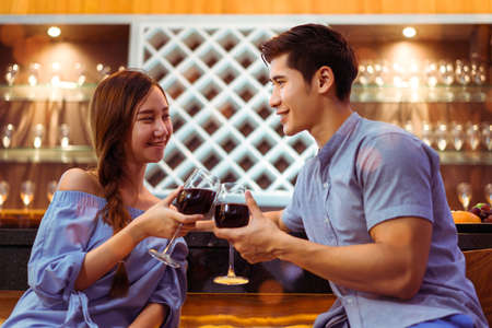 Young asian couple together man and woman clink glasses drink wine, cocktail in bar luxury party...