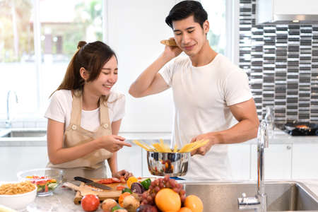 Young asian woman cutting slice vegetables making salad healthy food with fruits and man cooking menu for dinner in kitchen at home fun couple together romanticの写真素材