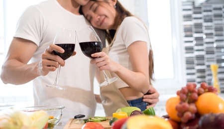 Young asian man and woman couple together holding wine glasses drinking after dinner in kitchen room at home lover romantic conceptの写真素材