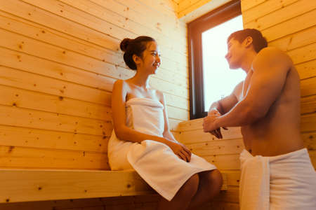 Young asian man and woman couple together sitting in sauna spa room with hot warm steam happy relaxing, resting for health care and skin in holiday at cabinの写真素材