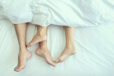 Closeup Feet of couple man and woman making love or sex on bed under blanket at hotel, home, sweet valentine concept.の写真素材
