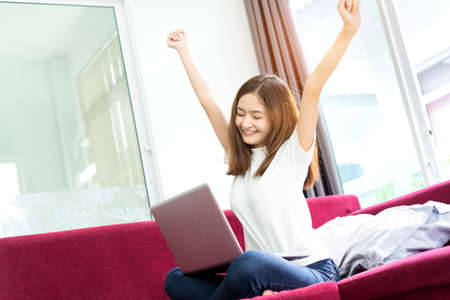 Young asian girl freelance lazy and happy success, finish, complete after working with laptop computer project in morning on sofa at home office in holidays.の写真素材