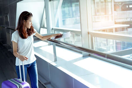 Young girl asian traveler walking with carrying hold suitcase luggage and passenger for tour travel booking ticket flight in airport international vacation time in holiday rest and relaxation.の写真素材