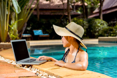 Woman bikini using laptop computer blank screen at swimming pool in resort edge relaxing hoildays