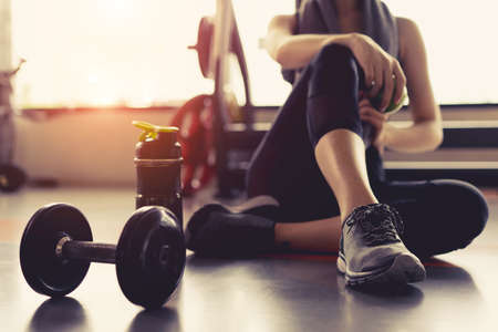 Woman exercise workout in gym fitness breaking relax holding apple fruit after training sport with dumbbell and protein shake bottle healthy lifestyle bodybuilding.の写真素材