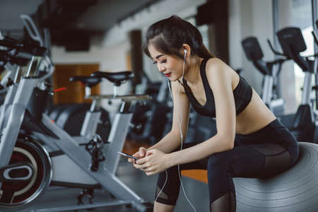 Young asian woman athlete listening music with smartphone relax after break workout and cardio sport...