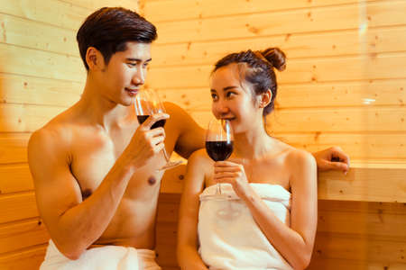 Couple at sauna spa healthy concept, Young asian man and woman together sitting in room with hot warm steam happy relaxing, resting for health care and skin in holiday with drinking cocktail, wineの写真素材