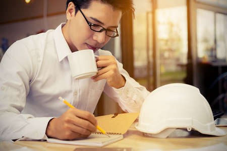 Engineer working business at office table with blueprint,paper plan,document,calculator drinking...