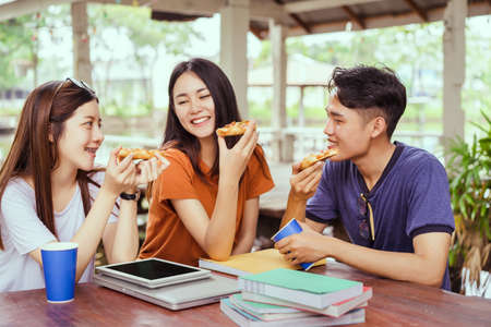 Students asian group together eating pizza in breaking time early next study class having fun and enjoy party italian food slice with cheese delicious at university outdoorの写真素材