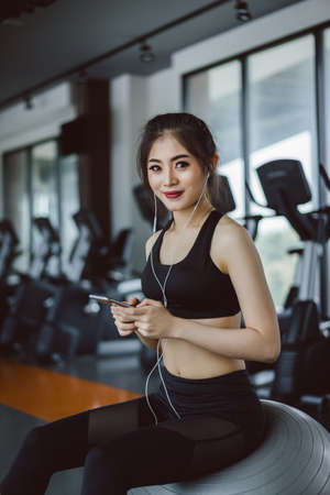 Young asian woman athlete listening music with smartphone relax after break workout and cardio sport...