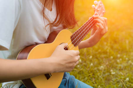 Closeup of girl playing ukulele in garden with acoustic guitar, young woman play music lifestyle classicの写真素材