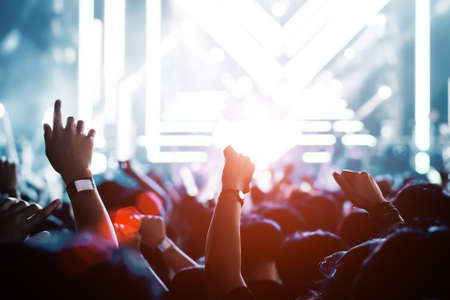 Crowd of hands up concert stage lights and people fan audience silhouette raising hands in the music festival rear view with spotlight glowing effectの写真素材