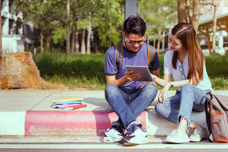 Students young asian together using laptop computer consult and reading book study smiling at university high school campus,college in summer holiday relaxationの写真素材