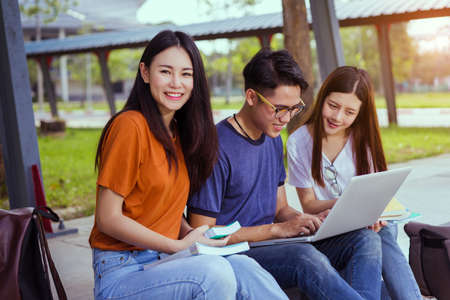 Students young asian together reading book study smiling with tablet,laptop computer at university high school campus,college in summer holiday relaxationの写真素材