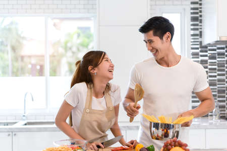 Young asian woman cutting slice vegetables making salad healthy food with fruits and man cooking menu for dinner in kitchen at home fun couple together romantic の写真素材