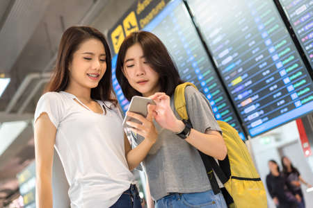 Asian friend together information board at airport for buy ticket flight travel vacation in holiday checking online by smartphoneの写真素材