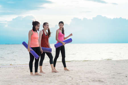 Asian women yoga teenager together talking on the beach with yoga mat at seaside after practice exercise healthy lifestyle sporty, Copy space the right.の写真素材