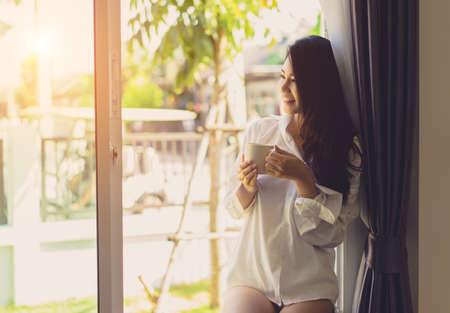 Asian woman drinking coffee in the morning breakfast in window bedroom fresh start the day happiness relax at home healthy lifestyle conceptの写真素材