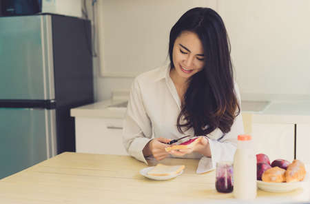 Asian woman slice jam bread in the morning and eating apple fruit,coffee healthy food breakfast meal in kitchen room fresh start the day at home healthy lifestyle conceptの写真素材