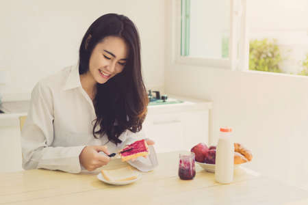 Asian woman slice jam bread in the morning and eating apple fruit,coffee healthy food breakfast meal in kitchen room fresh start the day at home healthy lifestyle conceptの写真素材