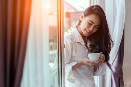 Asian woman drinking coffee in the morning breakfast in window bedroom fresh start the day happiness relax at home healthy lifestyle conceptの写真素材