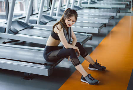 Asian woman sitting on treadmill after running exercise at gymの写真素材