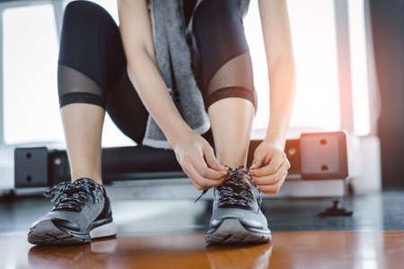 Woman knelt down to do up his shoelaces with protein shake at fitness gym after running exercise workout for cardio and muscle building.の写真素材