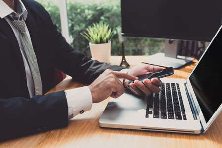Businessman using smartphone and laptop computer at workplace sitting update or report in email application earnings with networkの写真素材