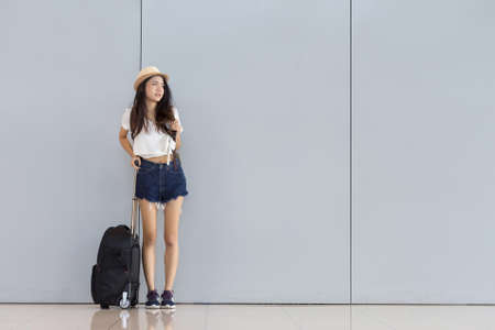 Asian woman teenager standing at airport terminal with luggage suitcase and backpack for travel in vacation summer relaxing waiting flight の写真素材