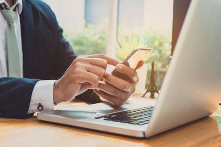 Businessman using smartphone and laptop computer at workplace sitting update or report in email application earnings with networkの写真素材