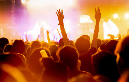 Crowd of concert stage lights and people fan audience silhouette raising hands or glow stick holding in the music festival rear view with spotlight glowing effect の写真素材