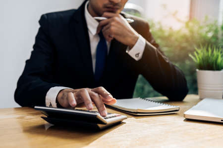 Businessman accouting management with calculator marketing report taking note balance of money statement on paperwork in office roomの写真素材