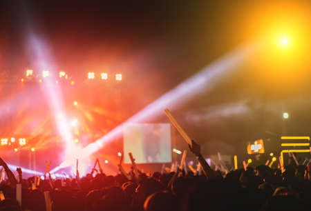 Silhouette crowd of concert stage lights and people fan audience raising hands or glow stick holding in the music festival rear view の写真素材
